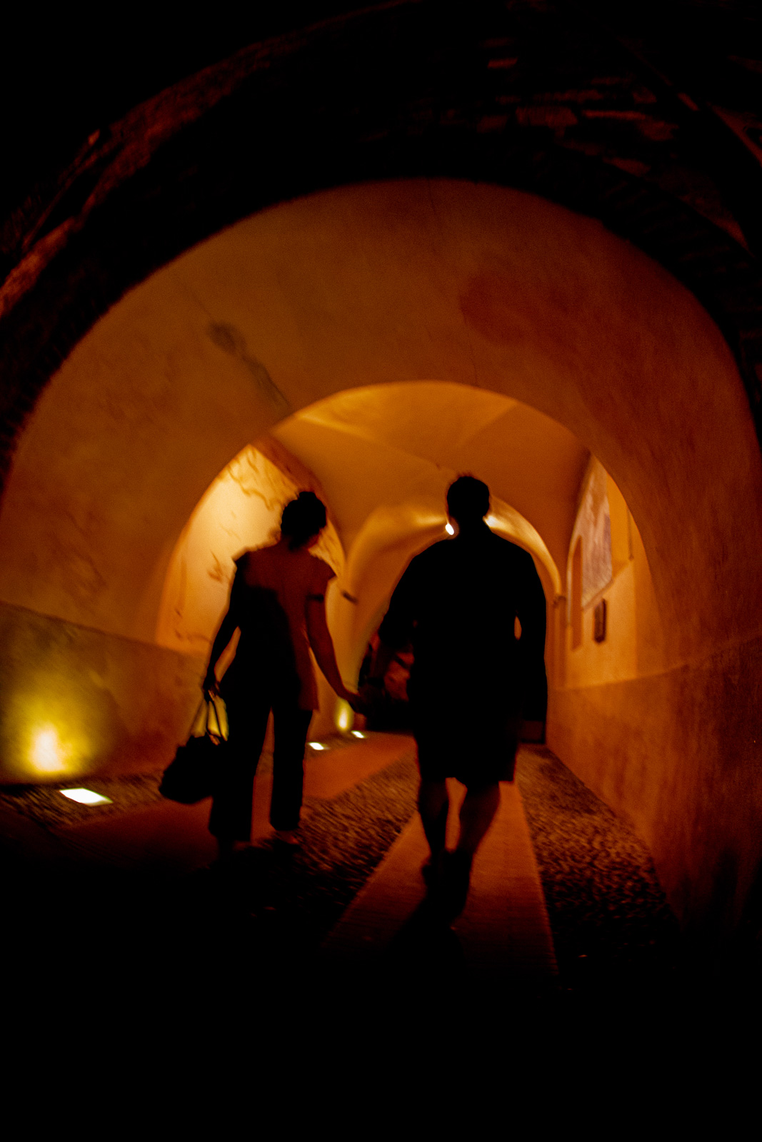 a couple walking through a tunnel in old world Italy, colors are orange and the poeple are a little blurry form movement indicating motion